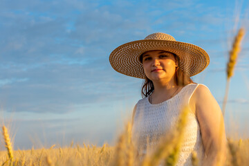 A woman in a sun hat stands happily in a wheat field under the bright sunlight