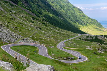 Car navigating mountain road with twists, surrounded by beautiful landscape