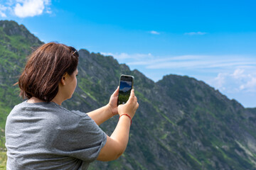 a woman is taking a picture of a mountain with her phone