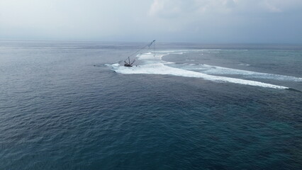 Fototapeta premium Aerial view of waves crashing on a sunken barge with a crane
