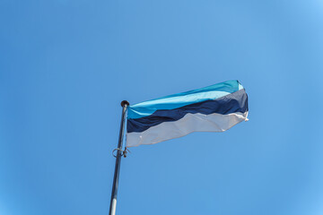 Estonian national flag waving on blue sky background. Republic of Estonia