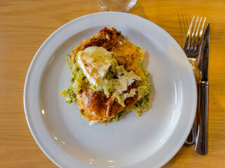 a slice, piece of a puff pastry pie filled with pesto and topped with oven-grilled goat cheese on a white plate with the utensils to the right on a hazelnut-colored wooden table."