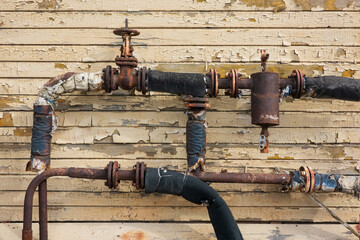 A fragment of an old rusty heating system made of pipes and valves against the background of the...