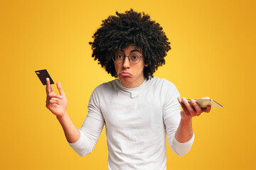 Upset black man holding bank card and smartphone