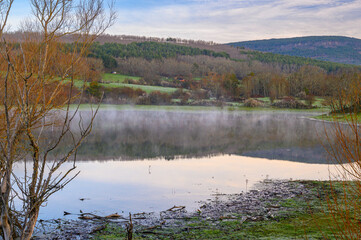 "A view of the mist rising from the water of a swamp, a lake, on a sunny but cold winter morning at the Pantano de la Cuerda del Pozo, Vinuesa, Spain."