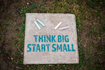 THINK BIG START SMALL. Colored pieces of chalk on a concrete pavement slab - 790980990