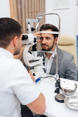 Attractive male doctor ophthalmologist is checking the eye vision of handsome middle age man in modern clinic. Doctor and patient during medical check up in ophthalmology clinic.
