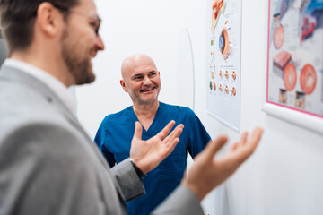 Handsome male patient standing and talking with good looking male doctor in a modern clinic for...