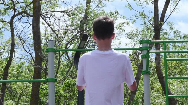 thin teenager, a schoolboy of 14 years old, plays sports on the playground, pulls himself up, does a warm-up. High quality 4k footage