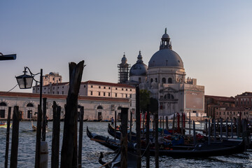Group of gondolas moored by Saint Mark square at sunset in city of Venice, Veneto, Northern Italy, Europe. Scenic view of Santa Maria Della Salute. Romantic vacation in the Venetian Lagoon - obrazy, fototapety, plakaty