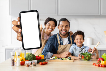 Positive African American family cooking together, showing smartphone