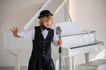 A young boy in a black vest and hat singing into a microphone.