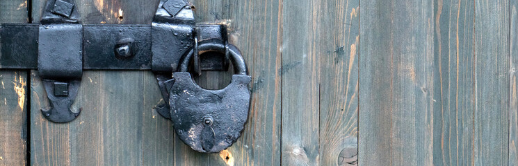 There is a rusty lock hanging on the wooden gate. Close-up view of a closed door. The wooden door...