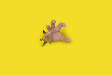 Hand of man coming out of torn yellow paper pretending to grab something. Space for text.