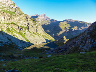 Scenic sunrise view of mountain summit Monte Viso (Monviso) and lake Lago Grande di Viso in the Cottian Alps, Piemonte, Italy, Europe. Rock walls of Stone king are shining in warm red orange colors
