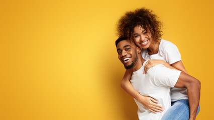 Happy african-american man and woman riding piggyback - obrazy, fototapety, plakaty