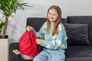 Morning preparation before school. Smiling Girl with Red Backpack on Couch. Back to school.