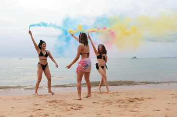 A young Woman's friends in bikinis   having fun with the smoke bomb on the beach on their summer vacation at a tropical sea
