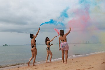 A young Woman's friends in bikinis   having fun with the smoke bomb on the beach on their summer vacation at a tropical sea