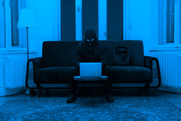 Burglar with laptop in a monochrome blue room