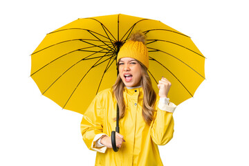 Young girl with rainproof coat and umbrella over isolated chroma key background celebrating a...