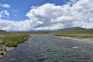 Breathtaking view of a river flowing through the vast deosai plains with mountains under a cloudy...