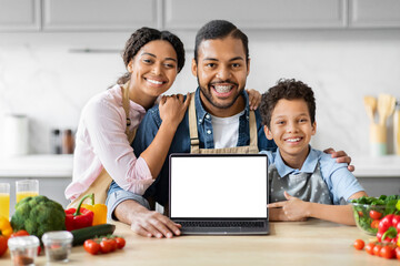 Positive African American family cooking together, showing laptop
