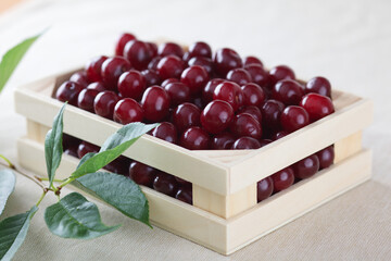 Small wooden crate full of fresh cherries on a beige cloth background.