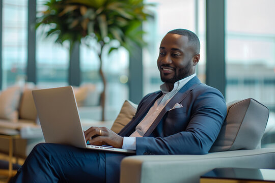 Black, African American man, businessman working on a laptop in a hotel lobby, waiting for someone, smiling