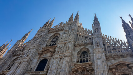 Fototapeta premium External view of Milan Cathedral (Duomo di Milano) from the Piazza del Duomo, Milan, Lombardy, Italy, Europe. Historical marble facade with spires. Gothic architecture features. City travel tourism