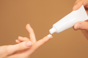 Woman's hand with a drop of cosmetic cream on top of finger groomed hands, natural short nails, on...