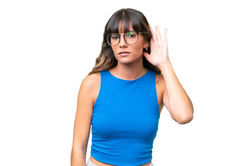 Young caucasian woman over isolated background listening to something by putting hand on the ear