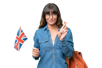Young caucasian woman holding an United Kingdom flag over isolated background with fingers crossing...