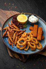 A plate of small deep-fried fish, squid rings and fish sticks.  Menu for a pub on a dark background. Colorful juicy food photography.