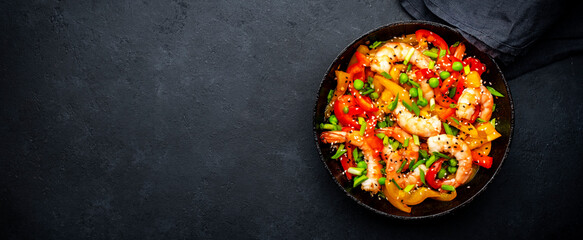 Hot stir fry shrimps with colorful paprika, green peas, chives and sesame seeds with ginger, garlic and soy sauce.   Black kitchen table background, top view - 791031354