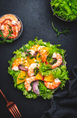 Fresh shrimp salad with orange, lettuce, cucumbers, red onion and sesame seeds with olive oil, black background, top view - 791031551
