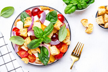 Salad with tomatoes, stale bread, onion, mozzarella cheese, green basil and olive oil, white table background, top view