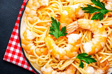 Ready for eat pasta with shrimp, olive oil and parsley on black table background. Top view