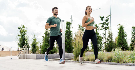 Joyful couple running in an urban park, showcasing a blend of fitness and modern landscape.