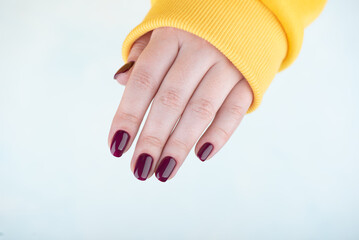 Woman's hand over light background with stylish blackberry color manicure on nails.