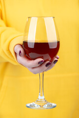 A woman's hand in a yellow sweater holds a glass of red wine.