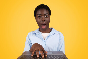 Black woman surprised at computer, yellow background