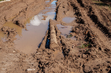 Closeup of country dirt road after rain,  dirty wooden log in puddle, sunny day