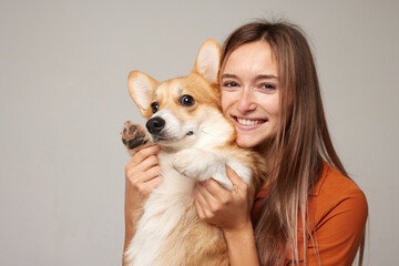 a brunette girl holds and hugs a red corgi dog on a clean light background, the concept of love for...