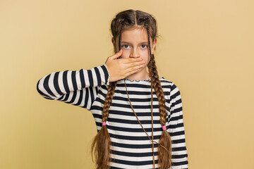 I will not say anything. Frightened child girl closing mouth with hands, looking intimidated scared at camera gestures no, refusing to tell terrible secret unbelievable truth. Kid on beige background