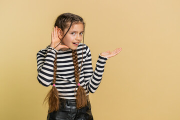 I cant hear you. What. Child girl kid trying hear you, looking confused and frowning, keeping arm near ear for louder voice asking to repeat to hear information deafness. Children on beige background