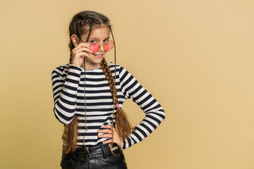Portrait of happy stylish young preteen child girl kid wearing sunglasses, charming smile, flirting, feeling very proud. Teenager children isolated on beige background indoors. People emotions concept