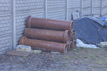 a pile of brown sewer ceramic pipes lie on the ground in green grass on the street near a gray...