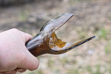 the hand of an aggressive criminal holds a piece of glass brown sharp broken bottle on the street