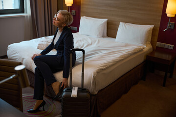 Caucasian businesswoman sitting on bed and putting on high heel in hotel room